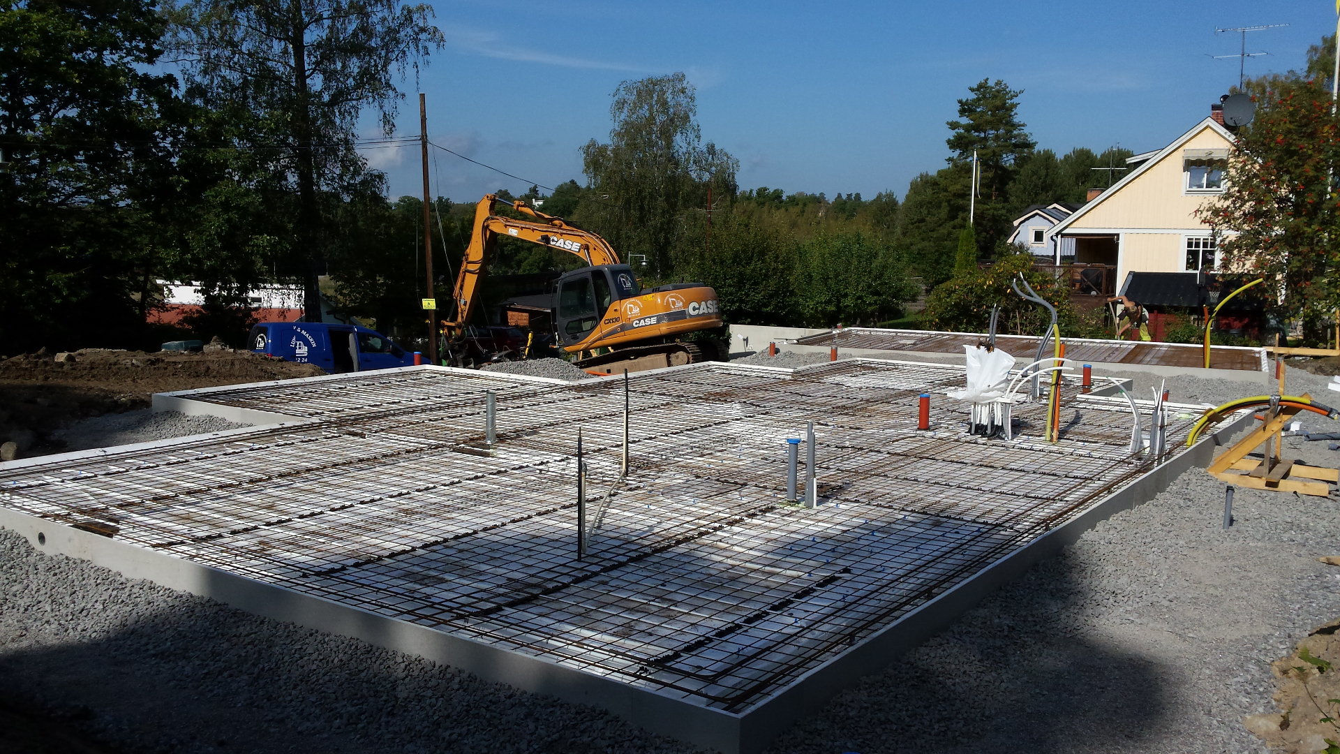 Villagrund med armering och grävmaskin